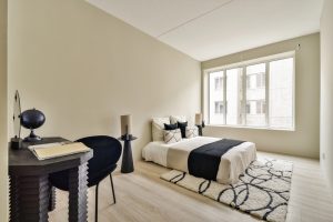 A sleek and modern bedroom featuring soft colors, minimal furniture, and large windows that bring in natural light, creating a cozy atmosphere.