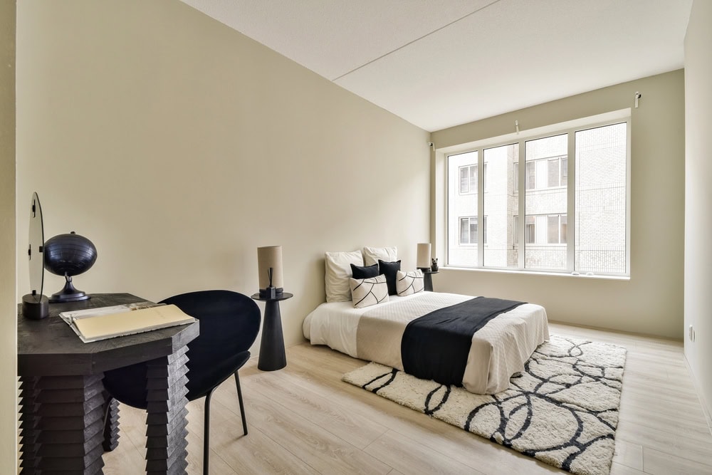 A sleek and modern bedroom featuring soft colors, minimal furniture, and large windows that bring in natural light, creating a cozy atmosphere.